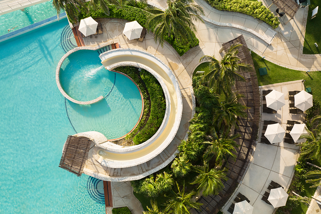 Aerial view of beautiful tropical resort with shimmering pools and many red deck chairs and umbrellas