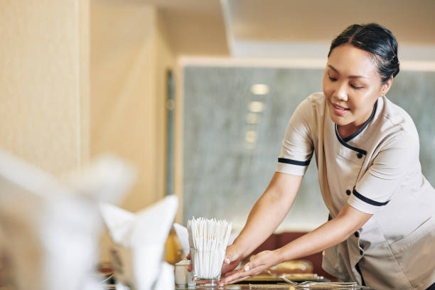 Housekeeping staff members in white uniforms making a bed with crisp white sheets